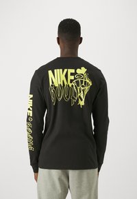 T-shirt a maniche lunghe nera con grafica e testo giallo sul retro e sulla manica destra. Realizzato in cotone con una vestibilità comoda.