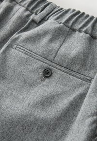 Gray fabric trousers with a relaxed waistband, featuring a back pocket and a single black button closure. The material appears textured.