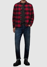 Camicia a quadri rossa e nera con bottoni sopra una t-shirt nera, abbinata a jeans blu scuro e stivaletti Chelsea neri. Maniche lunghe, vestibilità comoda.