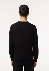 Maglione nero a maglia con maniche lunghe e scollo rotondo, caratterizzato da un orlo e polsini a costine, texture liscia e design aderente.