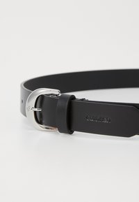Svart läderbälte med en glänsande silvrig metallspänne. Har en slät yta och ingraverad branding på remmen. Enkelt och funktionellt design.