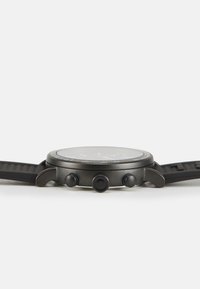 Reloj con correa de silicona negra, caja de acero inoxidable negro mate, tres botones de presión y un dial redondo con una esfera oscura y marcadores blancos.