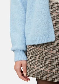 Jasnoniebieski sweter z dzianiny z ściągaczami na rękawach, połączony z brązową spódnicą w kratę z czarnymi i różowymi liniami. Miękka tekstura; dopasowany krój.