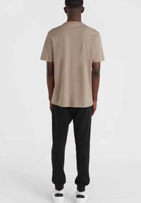 Beige Baumwoll-T-Shirt mit entspanntem Schnitt, kurzen Ärmeln und Rundhalsausschnitt, kombiniert mit schwarzen Jogginghosen und weißen Sneakers.