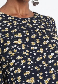 Granatowa sukienka w kwiaty z przypadkowym wzorem żółtych i białych kwiatów. Miękka tkanina, okrągły dekolt i subtelna tekstura.