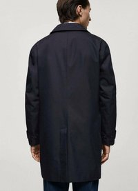Marinblå kappa med rak passform, tillverkad av mjukt tyg, med en bred krage och knappade manschetter, sedd bakifrån.