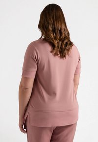 Top de manga corta y corte relajado en suave tela rosa, con una textura lisa, cuello redondo y aberturas laterales en el dobladillo para facilitar el movimiento.