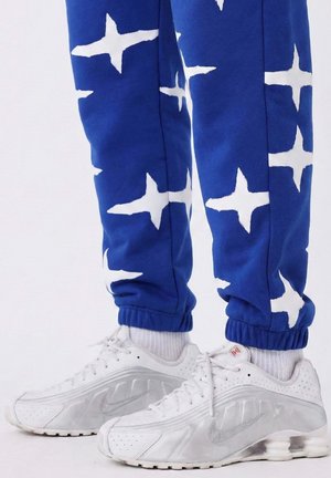 Blue sweatpants with white star patterns and elastic cuffs, paired with white and silver Nike sneakers featuring perforated details and laces.