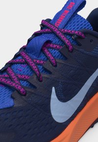 Přiblížení modro-oranžové běžecké boty Nike s růžovými a fialovými tkaničkami, prodyšným síťovaným svrchním dílem a logem Nike swoosh na boku.