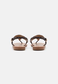Bruine leren sandalen met een platte zool, dunne banden en een gespsluiting. Het bovenwerk heeft een gladde textuur en een minimalistisch ontwerp.