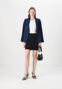 Marineblå dobbeltradet blazer, hvid ribbet bluse, sort skræddersyet nederdel med sølvdetaljer, sorte remsandaler og en struktureret sort håndtaske.