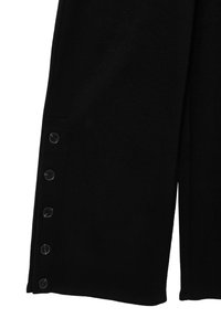 Schwarzes Stoffpanel mit vier schwarzen Knöpfen, die vertikal entlang der linken Kante ausgerichtet sind, und einen Teil eines Kleidungsstücks zeigend.