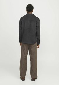 Dunkelgraues Langarmshirt mit entspannter Passform, ausgestattet mit einem spitzen Kragen und geradem Saum. Kombiniert mit lockeren beigen Hosen.