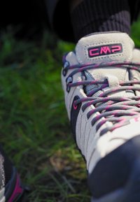 Scarpe da trekking grigie chiare con accenti neri, lacci rosa, pannelli in rete e una suola in gomma texture, appoggiate su erba verde.