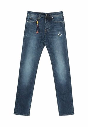 Niebieskie dopasowane dżinsy o prostym kroju z delikatnymi przetarciami na prawym udzie oraz dekoracyjnym breloczkiem z koralikami i materiałem wiszącym z przedniej lewej kieszeni.