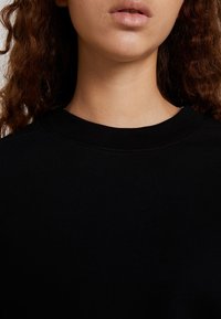 Sudadera de algodón negra con cuello redondo acanalado, de textura suave y sin patrones ni acentos visibles. Vista de cerca del escote y la parte superior del pecho.