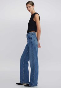 Top negro sin mangas con detalles texturizados, combinado con unos vaqueros de mezclilla azul de pierna ancha de cintura alta y tacones negros puntiagudos.