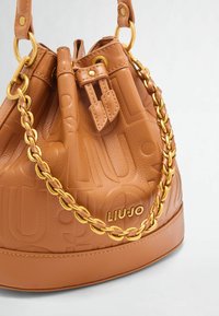 Braune Leder-Eimer-Tasche mit geprägtem Logo, goldfarbenen Beschlägen und abnehmbarem Kettenriemen. Verfügt über einen Kordelzugverschluss und eine strukturierte Oberfläche.
