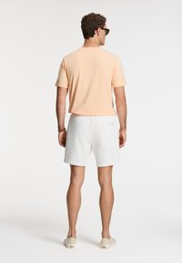 Kortærmet ferskenfarvet bomulds T-shirt kombineret med hvide shorts. Shortsene har en baglomme og et blødt, struktureret stof.