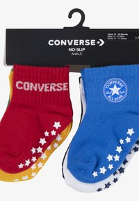Confezione di tre paia di calzini alla caviglia antiscivolo in rosso, giallo e blu. Presentano motivi a stella sulle suole e il marchio "Converse" sul calzino rosso.