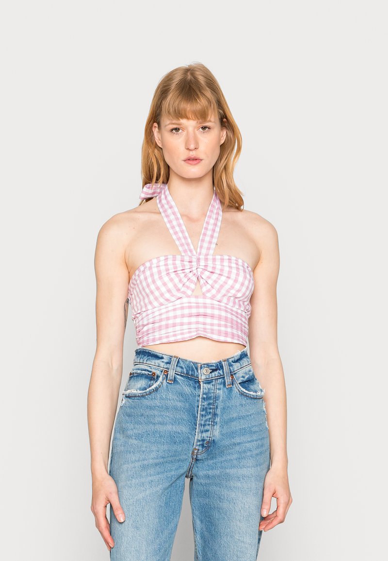 Top curto em gingham rosa e branco com decote halter e detalhe em nó na frente. Usado com jeans de denim azul desbotado com cintura alta.