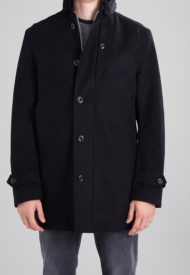 Cappotto di lana nero con colletto alto, bottoni frontali e tasche laterali. Tessuto morbido con polsini regolabili con bottoni.