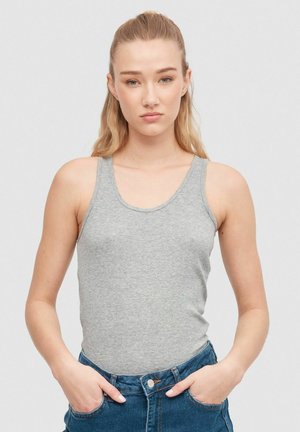 Top sin mangas gris de diseño ajustado, hecho de algodón acanalado. La modelo lo lleva con shorts de mezclilla de tiro alto, con las manos en los bolsillos.