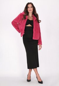 Giacca in pelliccia sintetica di un brillante rosa, con colletto arrotondato, abbinata a un vestito midi nero aderente con top attorcigliato e dettagli cut-out.
