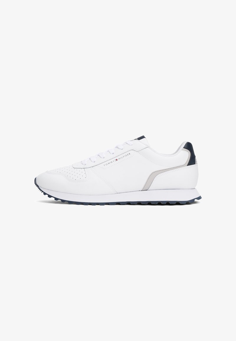 White sneakers made from smooth leather with perforated detailing, a contrasting navy heel, and a textured outsole for traction.