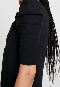 Černý krátký rukáv s jemnou texturou a nařaseným ramenním designem, s vykrojeným lemem a přiléhavým střihem.