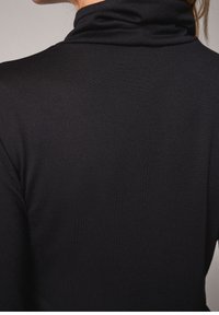 Pull col roulé noir présentant une texture douce, une coupe ajustée et un col roulé retroussé. Le tissu semble lisse et extensible.