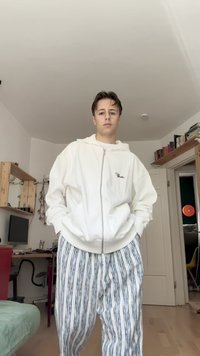 Bílá žebrovaná mikina na zip s dvěma předními kapsami, spárovaná se pruhovanými kalhotami s modrými a černými pruhy na bílém pozadí.