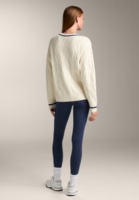 Cremfarbener Pullover mit strukturiertem Rautenmuster, gerippten Bündchen und Saum, kombiniert mit marineblauen Leggings und weißen Sneakern. Minimalistisches Design.