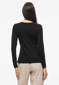 Czarna prążkowana bluzka z długim rękawem, o okrągłym dekolcie, dopasowanym kroju i teksturowanej tkaninie. W połączeniu z jasnobeżowymi spodniami.