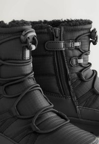 Bottes d'hiver noires avec un design matelassé, un matériau supérieur texturé, des lacets élastiques et une fermeture éclair sur le côté pour un enfilage facile.