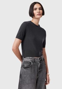 Kortærmet, cropped sweater i mørkegrå strikket stof med rund hals, parret med højtaljede, løstsiddende grå denimjeans.