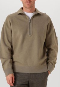 Hellbrauner Pullover mit einem halben Reißverschlusskragen, weicher Textur, gerippten Bündchen und Saum sowie einem subtilen tonalen Muster.