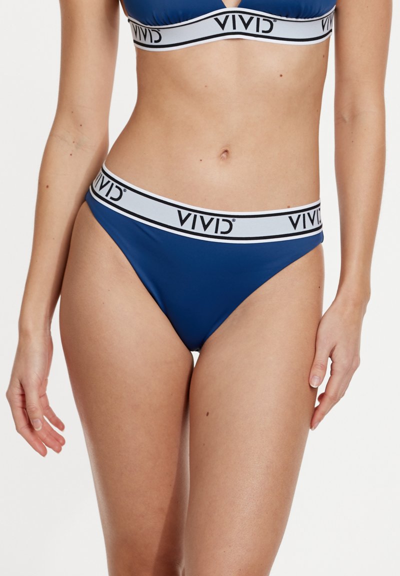 Zilā string apakšveļa ar platu baltu jostasvītru, uz kuras ir melns uzraksts "VIVID". Gluda auduma un minimālisma dizains.