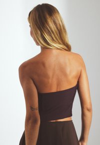 Dark purple strapless crop top, fitted design, textured fabric, with a smocked back. Hair partially visible, tattoo on arm.