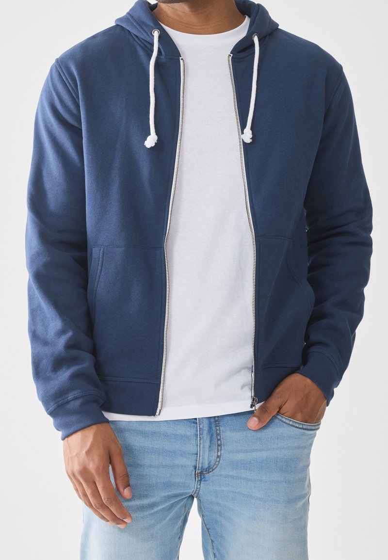 Marineblauwe zip-up hoodie met een trekkoordkap, twee voorzakken, ribgebreide manchetten en een witte binnenlaag die zichtbaar is eronder.