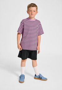 Lila-schwarz gestreiftes T-Shirt mit kurzen Ärmeln, schwarze Shorts und blaue Sneakers. Enthält weiße Socken und ein kleines Logo auf dem Shirt.