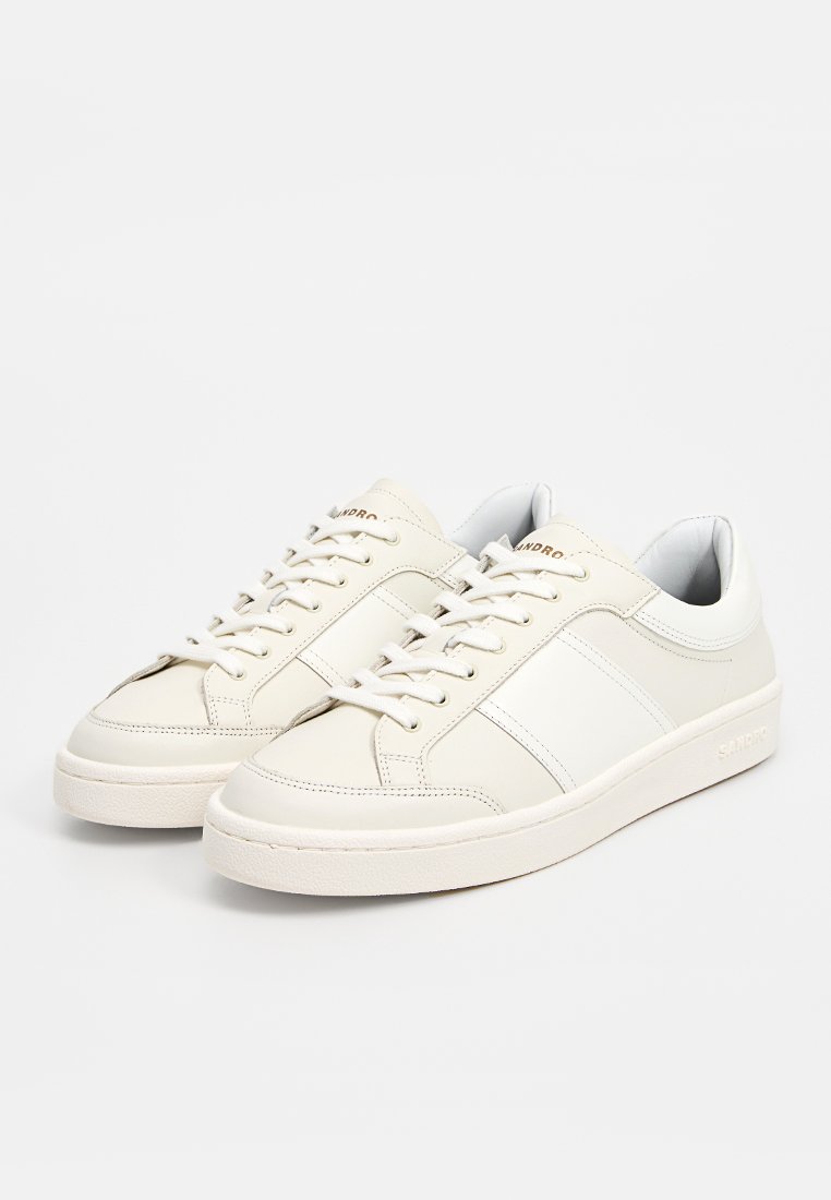 Witte leren sneakers met een gladde afwerking, ronde neus, platte veters en een minimalistisch ontwerp met beige accenten en merkbranding op de hiel.