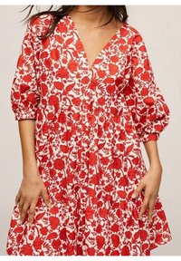 Robe rouge à motif floral avec un décolleté en V profond, des manches bouffantes, des boutons sur le devant et une jupe à volants, fabriquée en tissu léger.