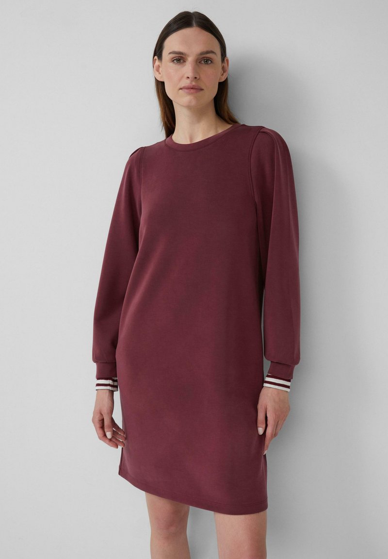 Bordeauxfarbiges Sweatshirtkleid mit langen Puffärmeln, gerippten Bündchen mit weißen und burgunderrot gestreiften Details sowie rundem Halsausschnitt. Angenehm glatte Oberfläche.