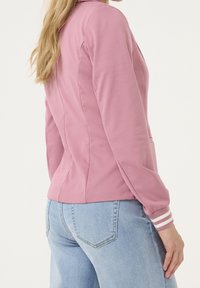 Sweat-shirt rose à coupe ajustée, avec un col plat et des poignets rayés. Associé à un jean bleu clair, présenté de profil.