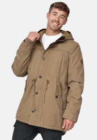 Veste kaki avec une capuche, des poignets côtelés et des doubles poches. Comprend un bouton frontal et une doublure texturée, avec des accents en cuir près des poches.
