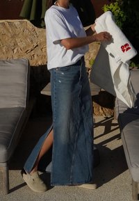 Denim maxikjol med sidoklipp, kombinerad med en vit t-shirt och ljusa träskor, håller en vit handduk med en röd design.