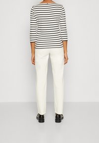 Pasiasty, długi rękaw, w kolorze kremowym i czarnym, zestawiony z białymi spodniami, o prostym kroju i postrzępionych brzegach, noszony z czarnymi butami.