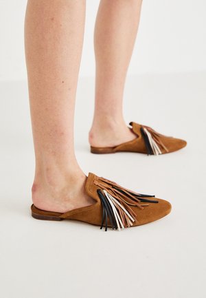Brown suede slip-on shoes featuring decorative multi-colored fringes in black, white, and brown. Flat sole with rounded toe design.