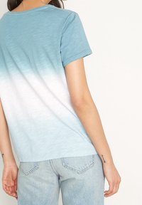 Kortärmad T-shirt i blå gradiente, som övergår från ljus till mörk. Mjuk, lättviktsmaterial med rundad halsringning och uppvikta ärmar.